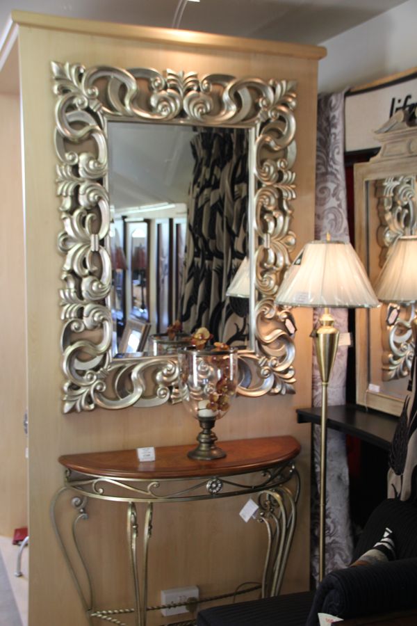 A console table with a mirror above it and a table lamp, styled as a hall setting in the showroom