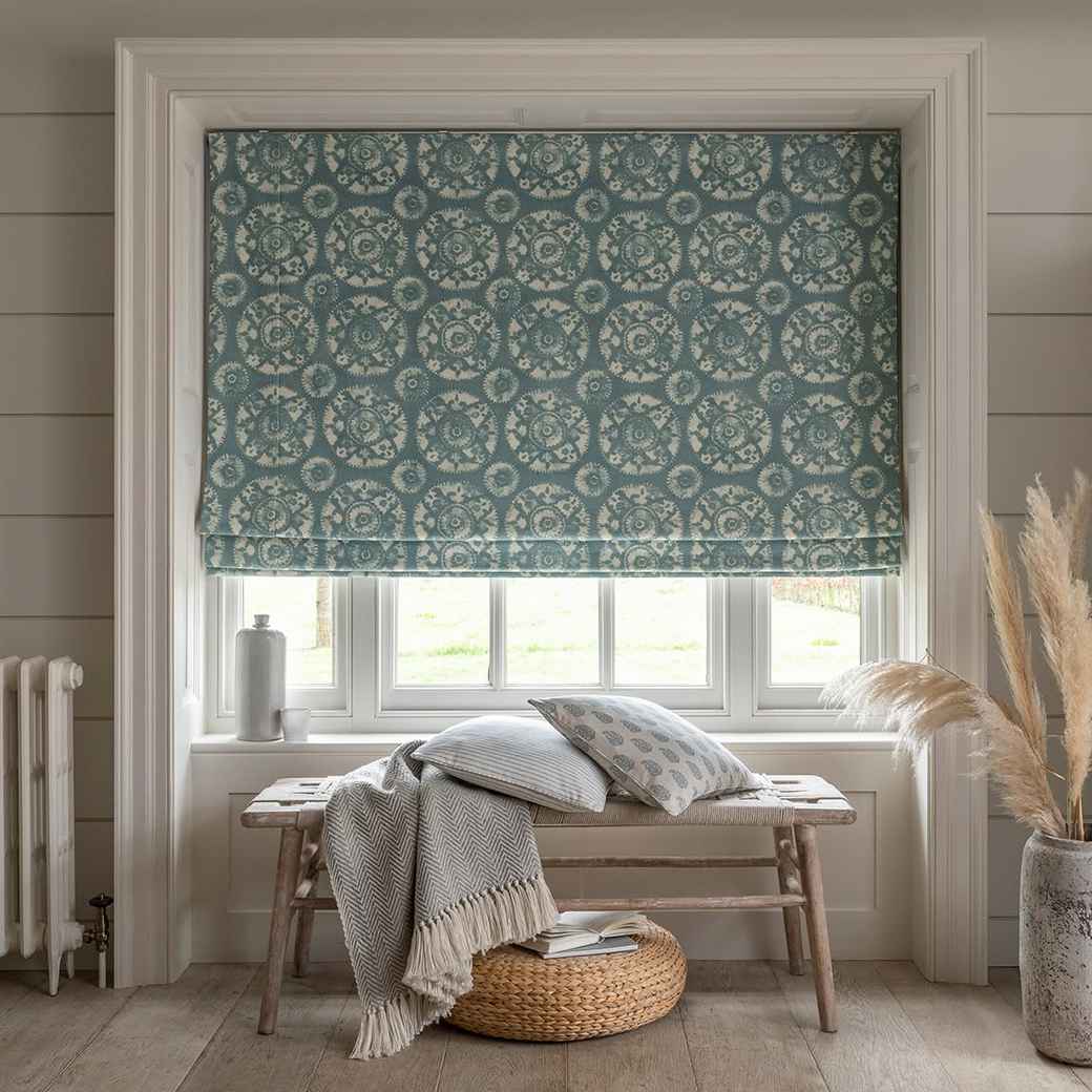 A patterned Roman blind fitted inside a window recess, pulled halfway up